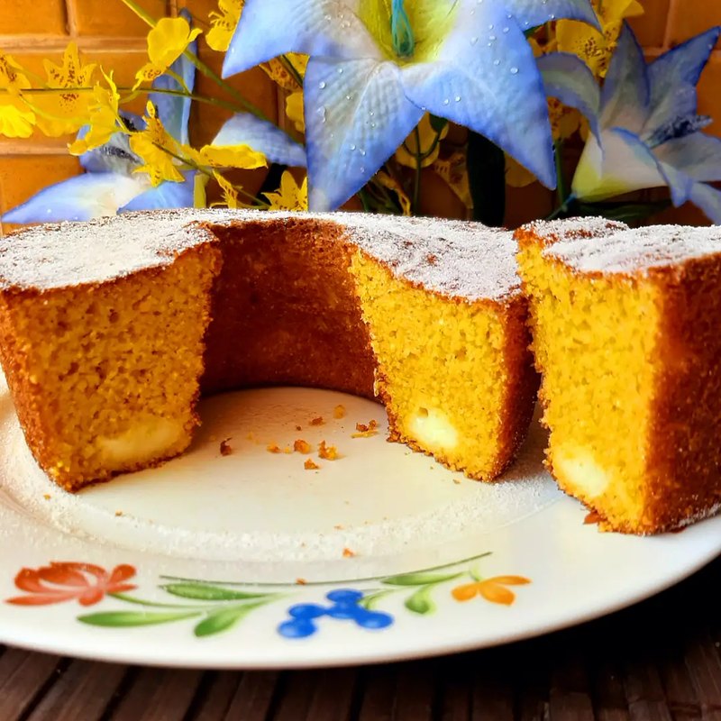 Bolo amarelo fatiado, com recheio cremoso aparecendo no corte, em prato floral