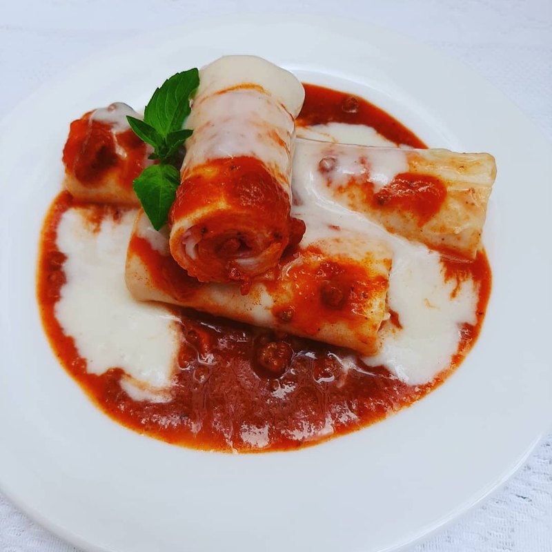 Canelones enrolados, servidos ao molho branco e vermelho em prato branco