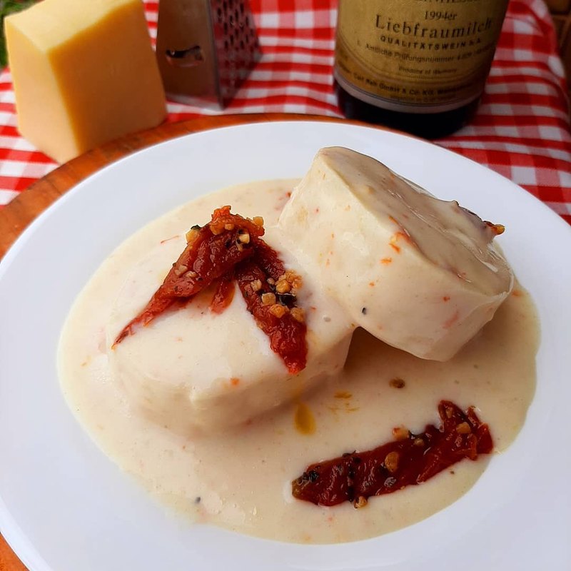 Rondeles ao molho branco com tomate seco, em prato fundo, ao lado de queijo e vinho