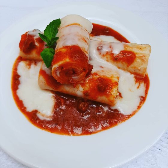 Canelones de presunto e muçarela ao molho, servidos em prato branco